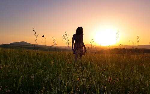 Eine Frau, die dem Sonnenaufgang entgegenläuft, sie trägt ein Kleid und hat lange Haare. | © pexels