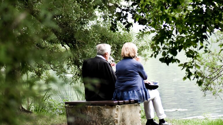 Ein älteres Paar sitzt auf einer Bank am See.  | © unsplash