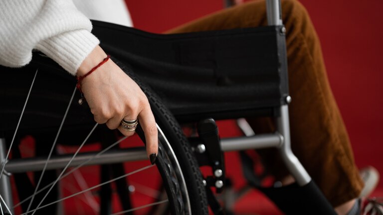 Nahaufnahme einer Frau im Rollstuhl, wobei man nur die Hand an den Rädern und die Beine sieht. | © Pexels / Shvets Production