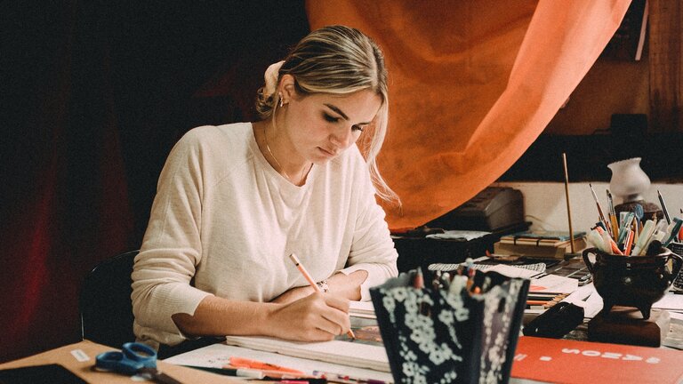 Eine Frau sitzt an einem Tisch und zeichnet ein Gemälde. | © unsplash