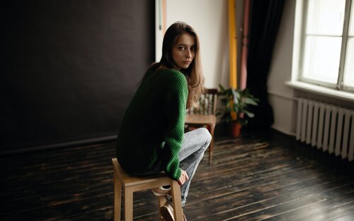 Eine Frau mit langen Haaren trägt einen grünen Pullover und sitzt auf einem Hocker. Sie schaut in die Kamera. | © unsplash