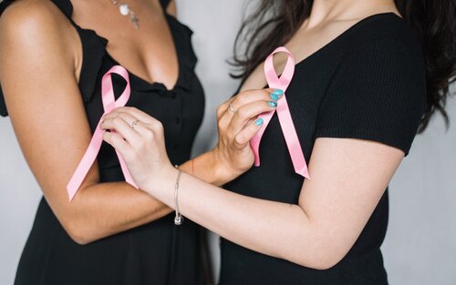 Zwei Frauen-Oberkörper in schwarzem T-Shirt. Sie halten die vordere Hand überkreuzt und halten ein rosa Schleifchen in die Kamera. | © pexels