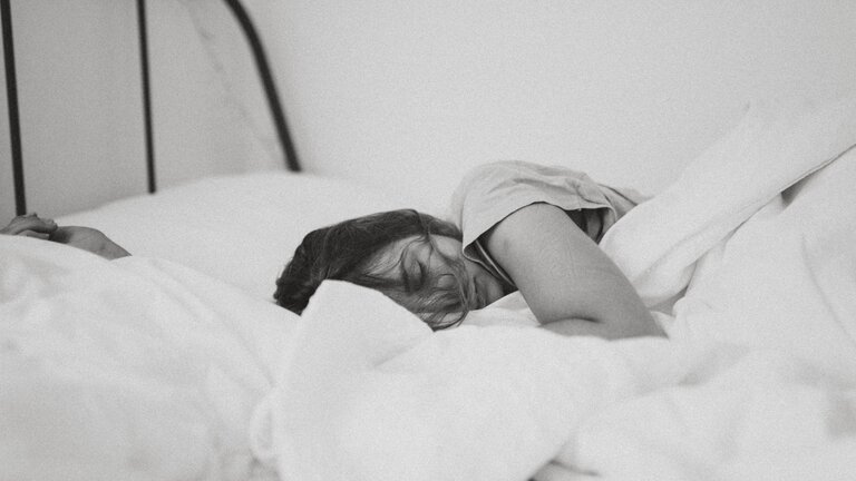 Aufnahme einer Frau, die seitlich und zugedeckt im Bett liegt und schläft. | © unsplash
