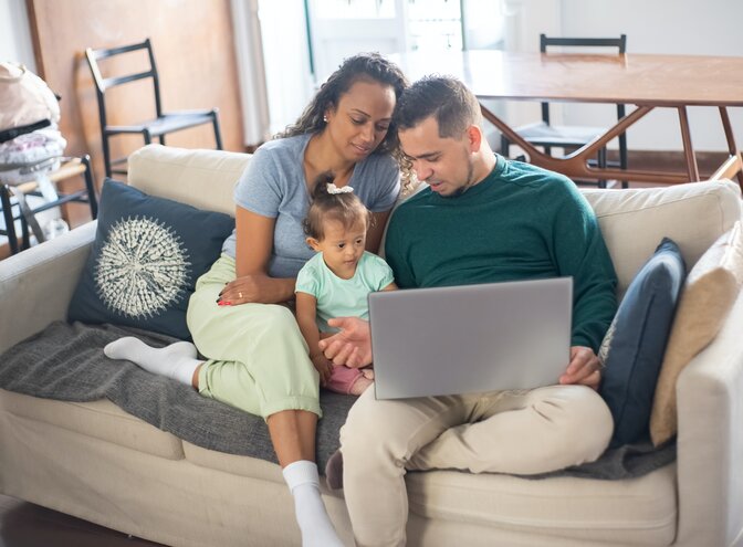 Eltern sitzen mit ihrer kleiner Tochter und einem Laptop auf den Knien auf dem Sofa und informieren sich. | © Pexels / Kampus Production