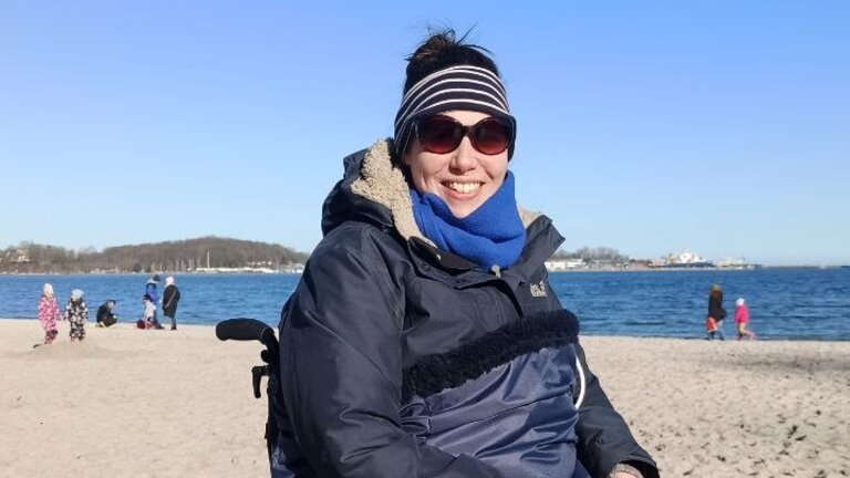 Wiebke im Rollstuhl am Strand mit einer Decke, Stirnband und Sonnenbrille | © Privataufnahme