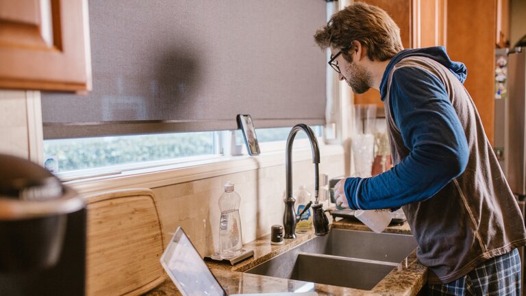 Ein Mann beim Abwasch, der gleichzeitig telefoniert und den Laptop geöffnet hat. | © pexels