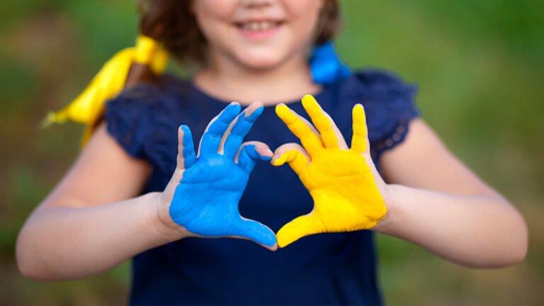 Ein Mädchen, dessen Hände in blau und gelb angemalt sind, formt ein Herz. | © pexels