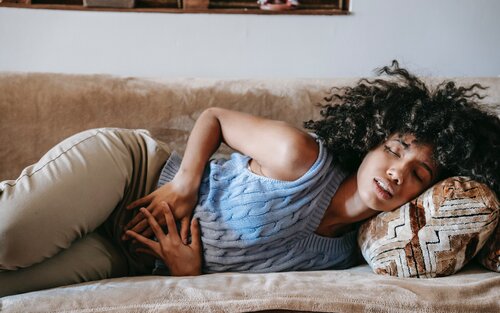 Bild einer Frau, di auf einem Bett liegt und die Hände an ihren Bauch presst. Sie hat offensichtlich Schmerzen. | © pexels
