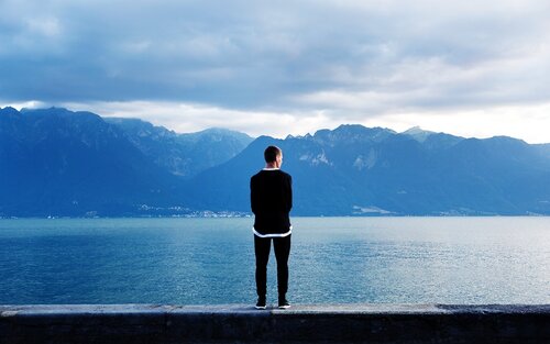 Homme de dos debout sur un mur regardant un lac | © pixabay