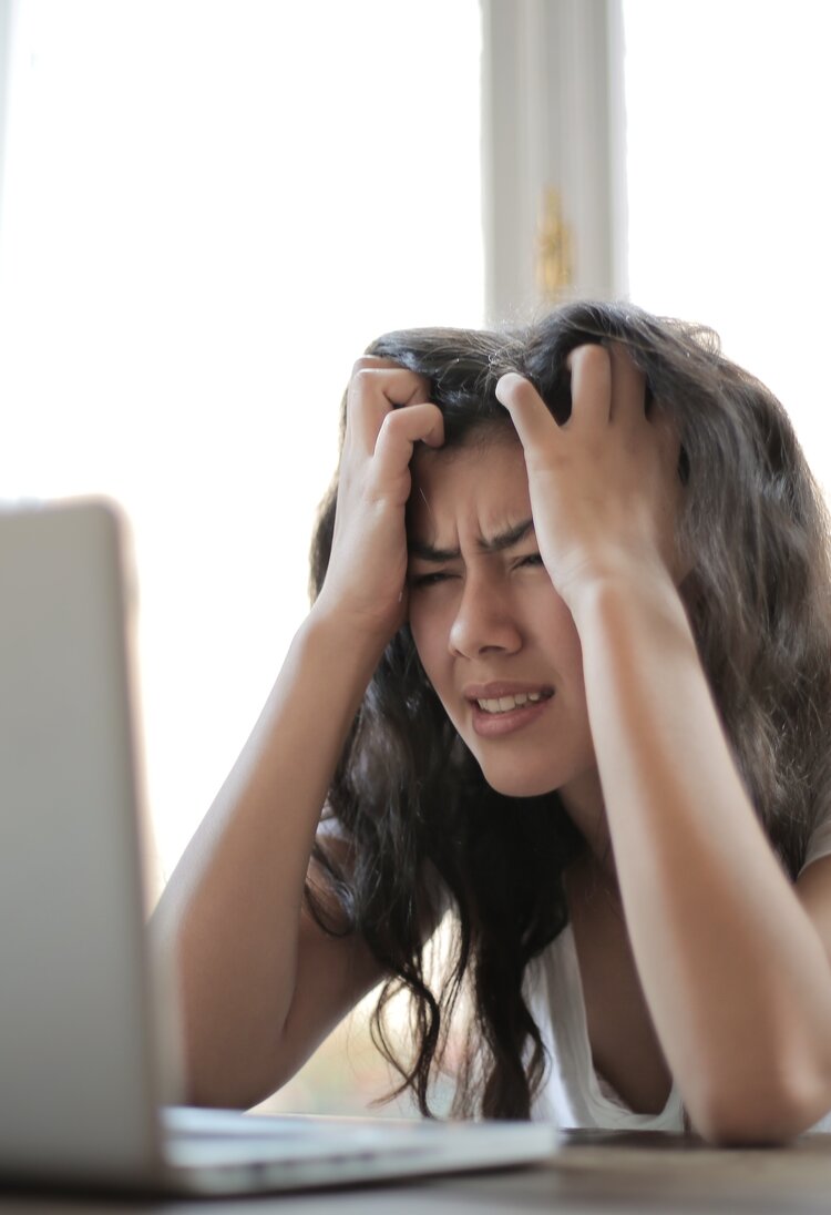 Eine Frau im weissen Shirt sitzt am Laptop und rauft sich die Haare. Sie ist offensichtlich gestresst. | © Pexels/Andrea Piacquadio