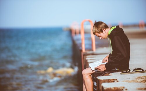 Junge sitzt alleine an der Küste und schaut ins Meer. | © unsplash