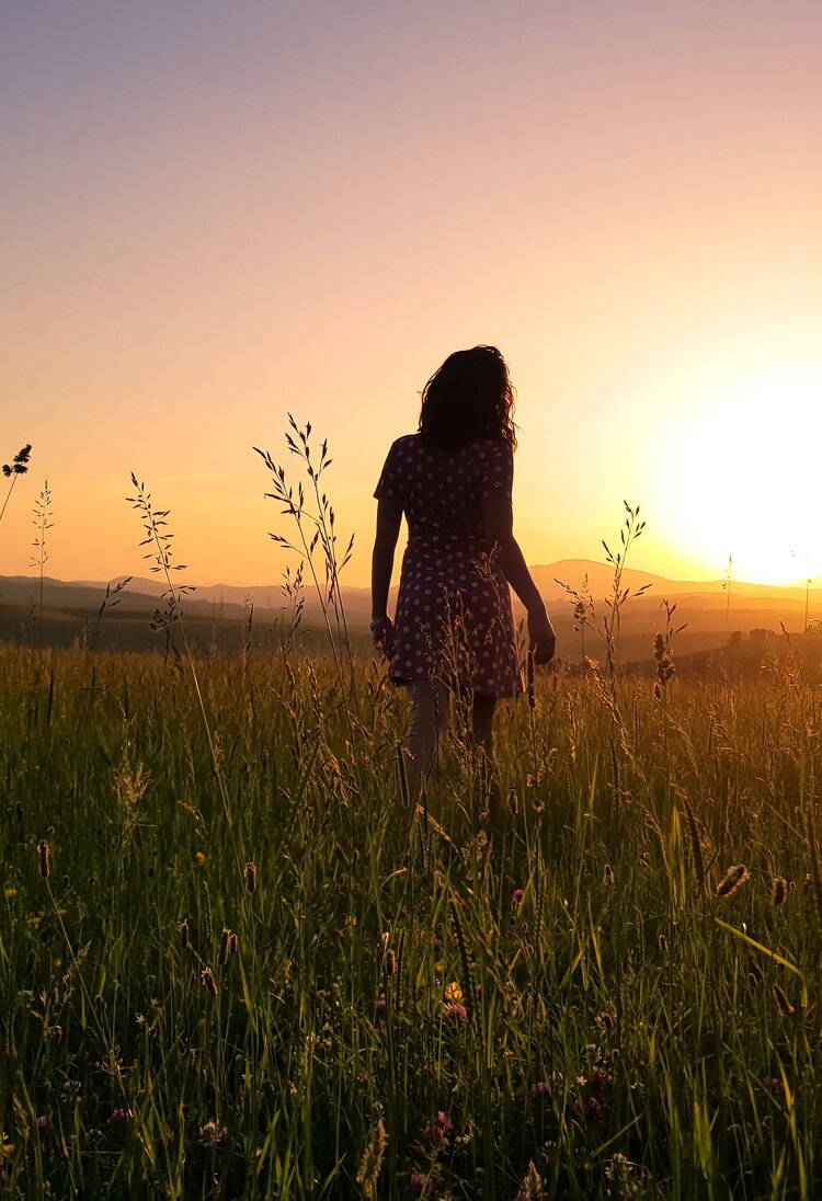 Eine Frau, die dem Sonnenaufgang entgegenläuft, sie trägt ein Kleid und hat lange Haare. | © Pexels/Marinko Krsmanovic