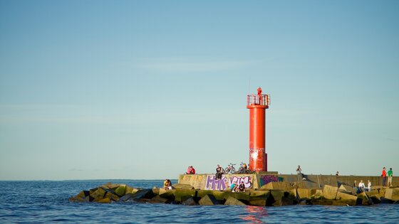 Ein roter Leuchtturm neben dem Meer mit Personen auf den Felsen um ihn herum verstreut | © Unsplash