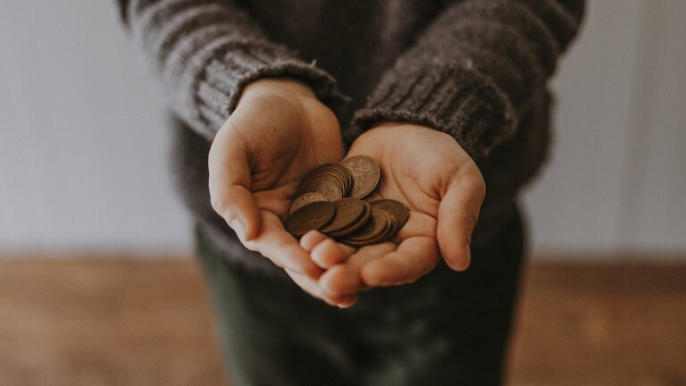 Nahaufnahme eines Kindes, das Münzen in der Hand hält. | © unsplash