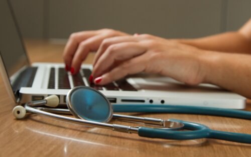 Nahaufnahme der Hände einer Person, die etwas in den Laptop eintippt, ein Stethoskop daneben. | © unsplash