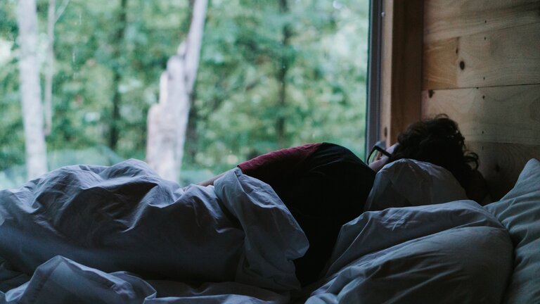 Von hinten fotografierter Mann liegt deprimiert im Bett | © unsplash