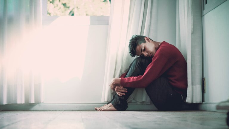 Ein deprimierter Mann sitzt unter einem Fenster. | © unsplash