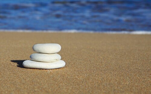 Drei runde Steine mit von oben nach unten ansteigender Grösse, die übereinander auf Sand mit dem Meer im Hintergrund gestapelt sind. | © pixabay