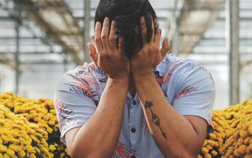 Bild eines Mannes, der inmitten von Blumen sitzt und den Kopf in die Hände gestützt hat. Er weint offensichtlich. | © pexels