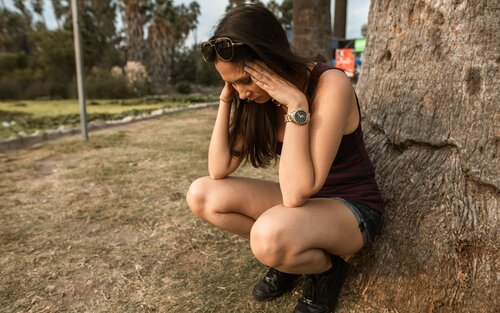 Bild von einer Frau, die in einem Park auf dem Boden sitzt. Ihre Hände bedeckten ihr Gesicht, sie ist sichtlich verängstigt. | © pexels