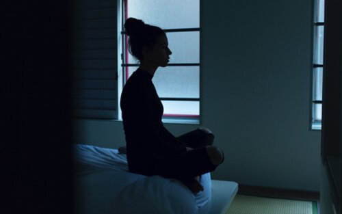 Eine Frau sitzt auf einem Bett und schaut aus dem Fenster. | © unsplash