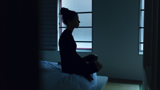Eine Frau sitzt auf einem Bett und schaut aus dem Fenster. | © unsplash