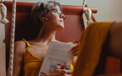 Eine Frau hält ein Buch in den Händen und schaut nachdenklich in die Ferne. | © pexels