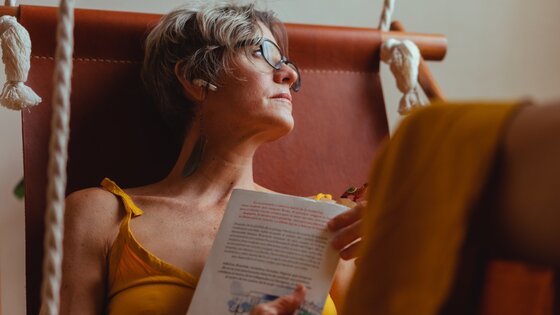 Eine Frau hält ein Buch in den Händen und schaut nachdenklich in die Ferne. | © Pexels / Los muertos crew