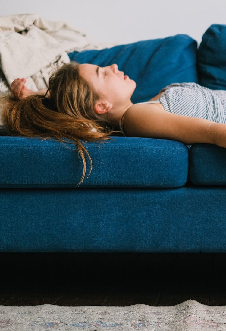 Eine Frau liegt müde auf dem Sofa und starrt erschöpft an die Decke. | © Pexels / Shvets Production