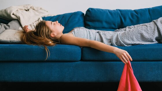 Eine Frau liegt müde auf dem Sofa und starrt erschöpft an die Decke. | © Pexels / Shvets Production