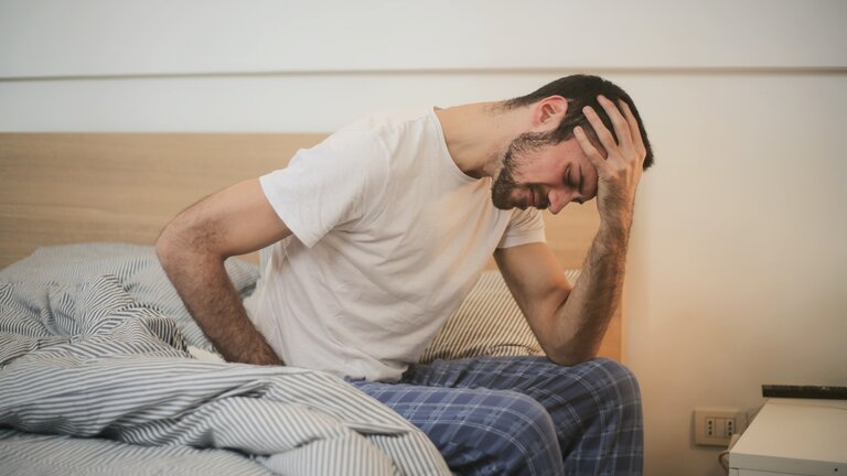 Ein Mann sitzt am Rand seines Bettes und stützt erschöpft und frustriert den Kopf auf. | © Pexels / Andrea Piacquadio