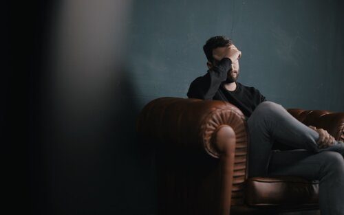 Ein Mann sitzt auf dem Sofa und hält sich die Hand vor das Gesicht. | © unsplash