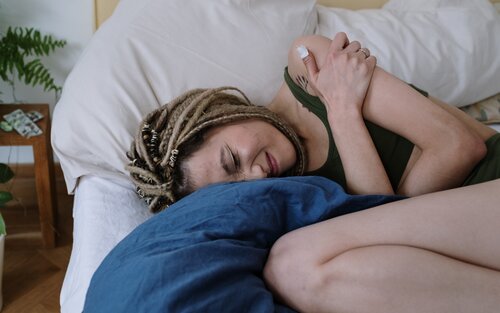 Eine Frau liegt mit starken Bauchschmerzen in Embryostellung im Bett. | © Pexels / Cottonbro Studio