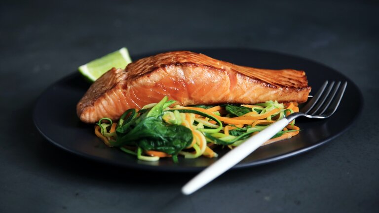 Auf einem schwarzen Teller ist Lachs mit Gemüse und eine Gabel.  | © Unsplash