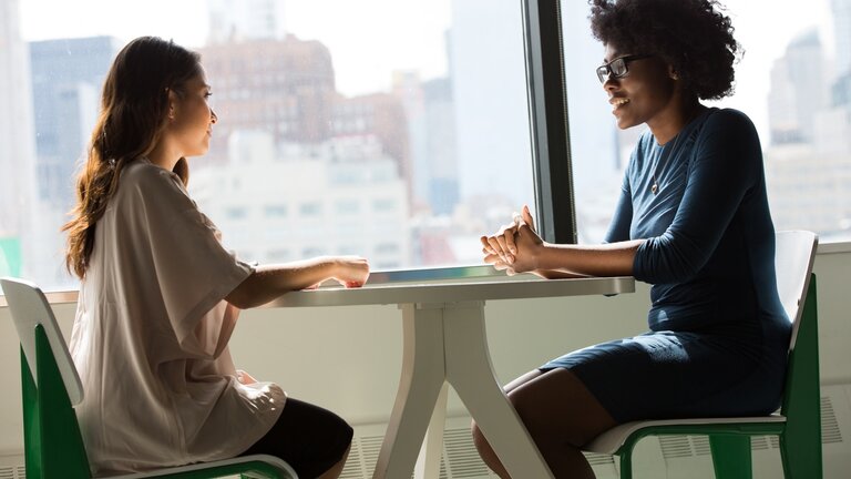 Zwei Frauen sitzen an einem Tisch und führen ein Gespräch. | © unsplash