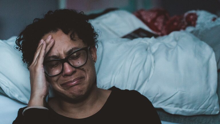 Eine weinende Person sitzt vor einem Bett auf dem Boden. | © unsplash