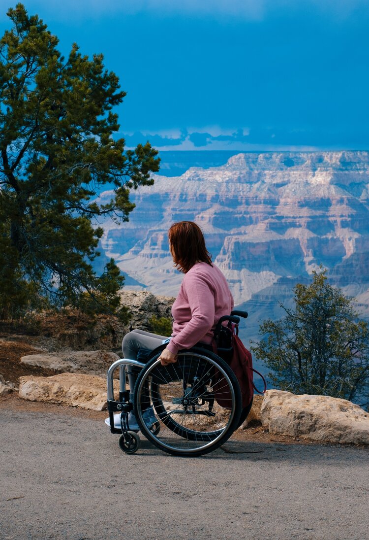Auf dem Bild ist eine junge Frau zu sehen, die im Rollstuhl sitzt. Sie schaut auf ein Tal hinab. | © Unsplash