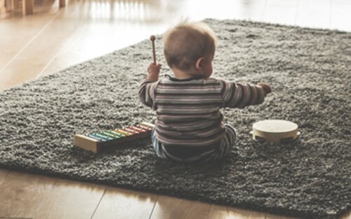 Ein kleines Kind sitzt auf einem Teppich und spielt mit Musikinstrumenten. Im Hintergrund ist eine Wohnzimmereinrichtung zu erkennen. | © Pixabay