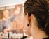 Junge Frau von hinten mit Hörgerät sieht auf ein verschwommenes Plakat. | © Gesellschaftsbilder.de