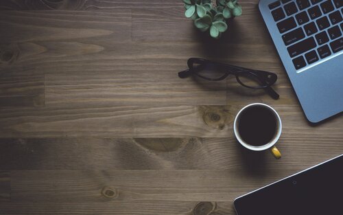 Auf einem braunen Tisch ist ein Laptop, eine schwarze Brille, eine Tasse Kaffee und eine kleine grüne Pflanze. | © pixabay