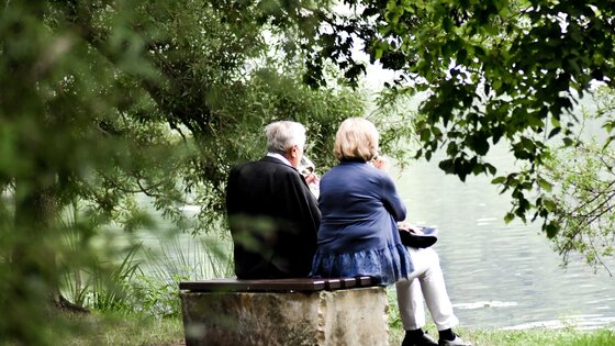 Un couple de personnes âgées est assis sur un banc au bord du lac.  | © Unsplash