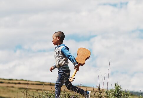 Junge rennt über Wiese mit Ukulele in der Hand. | © unsplash