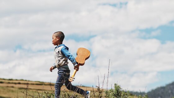 Junge rennt über Wiese mit Ukulele in der Hand. | © Unsplash