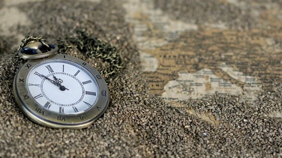 Eine Taschenuhr auf einer Weltkarte umgeben von Sand.  | © Pixabay