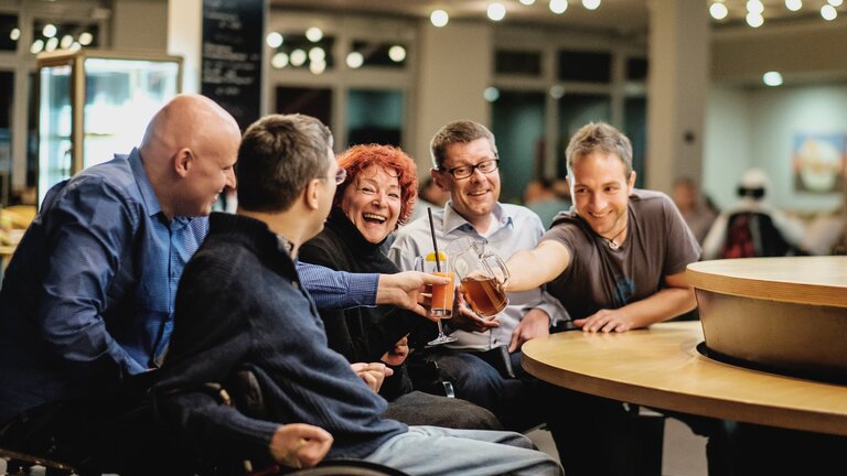 Menschen mit Behinderungen in Interaktion mit ihren Assistenzen in einer Bar. | © Andi Weiland | Gesellschaftsbilder.de