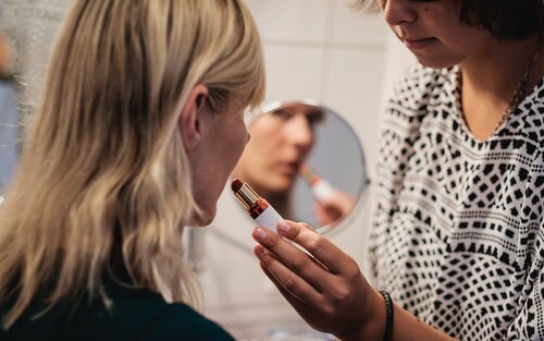 Assistenzperson hilft Frau mit einer Behinderung bim Auftragen von Lippenstift. | © Andi Weiland | gesellschaftsbilder.de