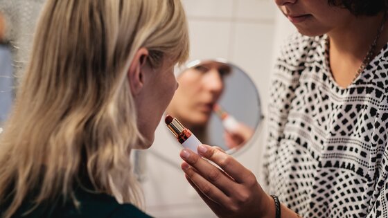 Assistenzperson hilft Frau mit einer Behinderung bim Auftragen von Lippenstift. | © Andi Weiland | Gesellschaftsbilder.de