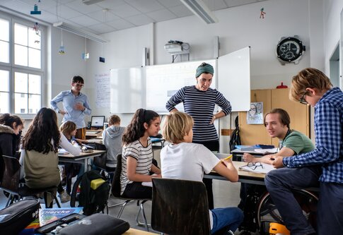 Ein Schüler im Rollstuhl an einer inklusiven Schule spricht mit anderen Schüler:innen und einer Lehrerin. | © Andi Weiland, Gesellschaftsbilder.de