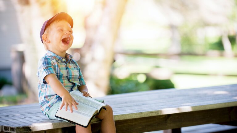 Ein Junge mit einem Buch lacht.  | © Unsplash