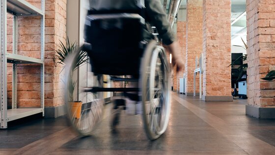 Rollstuhl fährt schnell durch ein Büro. Person im Rollstuhl ist nicht erkennbar. | © Pexels / Marcus Aurelius